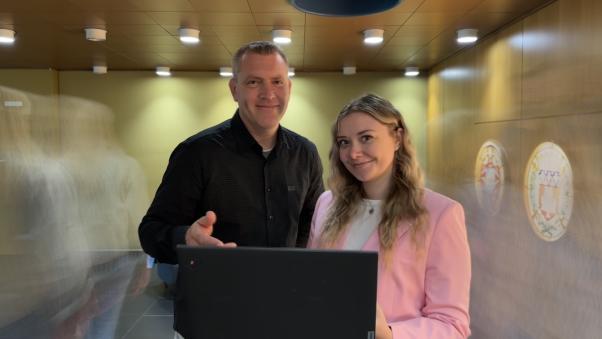 Zwei Menschen schauen, halten Laptop, unscharfe Menschen ziehen vorbei