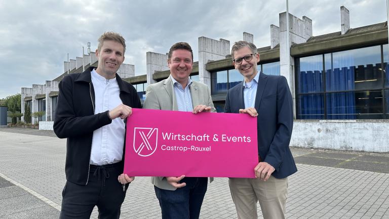 Drei M&auml;nner halten Schild mit neuem Logo der Wirtschaft & Events GmbH